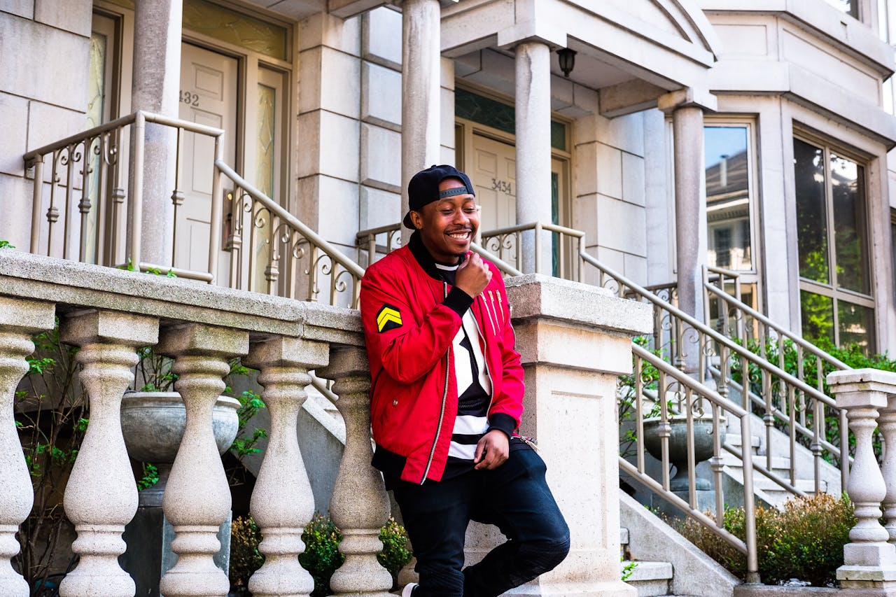 A cheerful man in casual streetwear posing on a porch with a stylish facade.