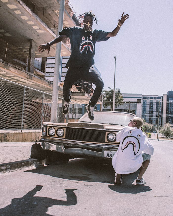 Man jumps in urban setting showcasing streetwear fashion with vintage car.