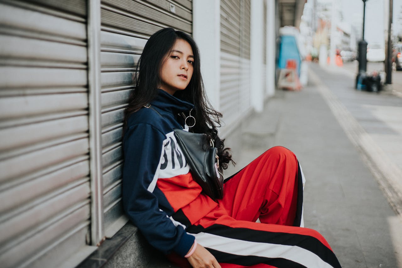 A young woman in streetwear poses casually against city backdrop, showcasing urban fashion vibes.